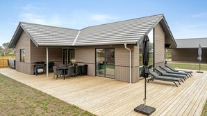 Una casa moderna con un porche cubierto, zona de barbacoa y mobiliario de exterior.