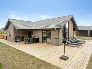 Ein modernes Haus mit überdachter Terrasse, Grillplatz und Gartenmöbeln.