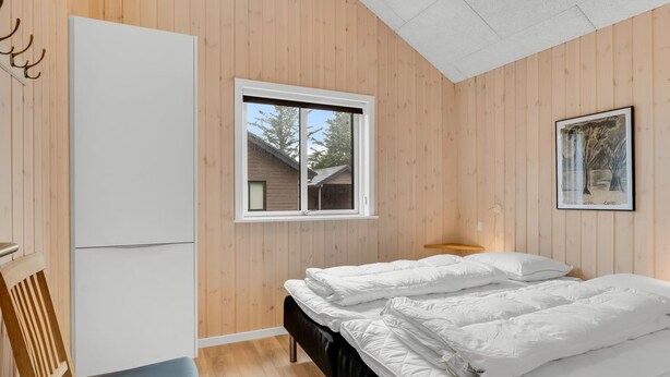 Un dormitorio con una cama, una silla, un ventanal y un cuadro colgado en la pared.