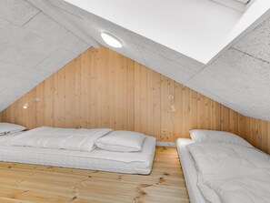 Una habitación con dos camas, paredes de madera y un techo inclinado con tragaluz.