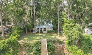 A house surrounded by dense trees and a wooden deck leading to the front porch.
