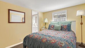 Ein Schlafzimmer mit Bett, Nachttisch, Lampe, Fenster mit Jalousien und einer Tür.