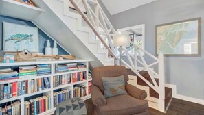 Eine Treppe mit weißen Geländern, ein Bücherregal mit Büchern, ein Sessel mit Kissen und eine gerahmte Karte an der Wand.
