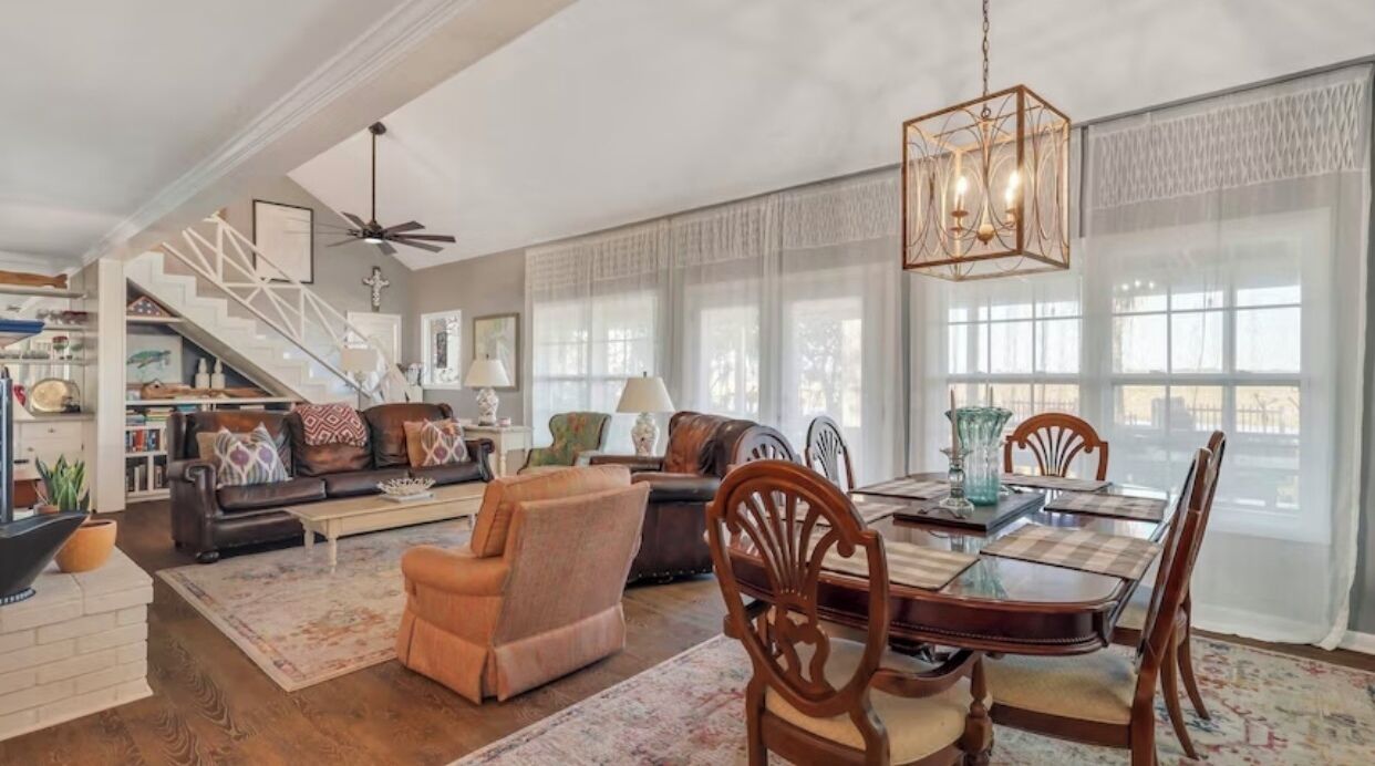 A spacious living room with a dining area, a staircase, and large windows.