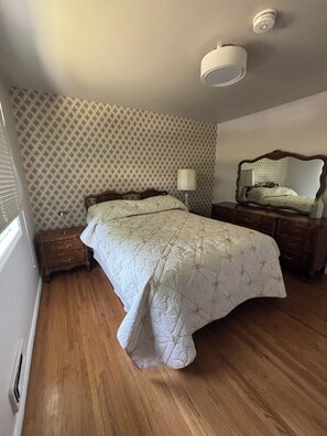 Ein Schlafzimmer mit einem großen Bett, einem Schminktisch, einem Nachttisch, einer Lampe und einem Spiegel.
