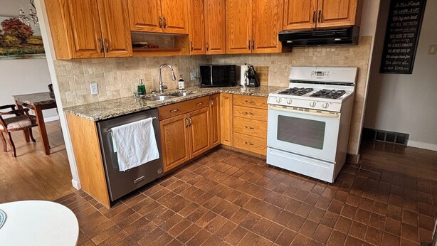 Una cocina con armarios de madera, estufa, microondas y pileta.