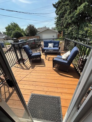 Eine Holzterrasse mit Gartenmöbeln, darunter zwei Sofas und ein Tisch, umgeben von einem Metallgeländer.