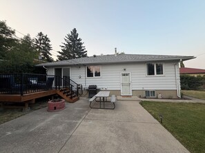 Une maison de plain-pied avec un patio, un barbecue et une petite terrasse avec des chaises.