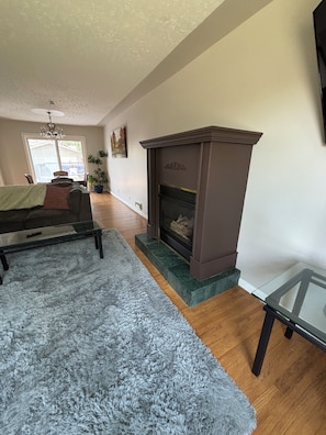A living room with a fireplace, a glass coffee table, a fluffy rug, and a dining area with chairs and a table. - Cozy home away from home in NW Calgary. Great location and has all amenities (Calgary)