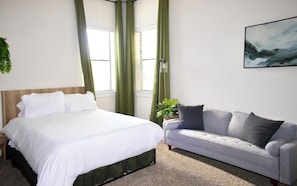 Ein Schlafzimmer mit einem Bett, einem grauen Sofa, einer Topfpflanze und einem Bild an der Wand.