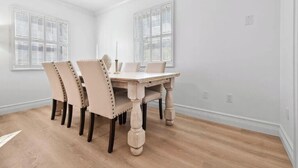 Un comedor con una mesa de madera y cuatro sillas, paredes blancas y dos ventanas con contraventanas.