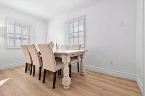 Ein Esszimmer mit Holztisch und vier Stühlen, weißen Wänden und zwei Fenstern mit Fensterläden.