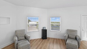 Una habitación con dos sillones estampados, una mesita auxiliar negra y dos ventanas con persianas.