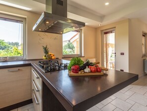 A modern kitchen with a gas stove, a large island with fresh produce, and a view of greenery outside. - in Medulin mit Privatem Pool by Interhome (Medulin)