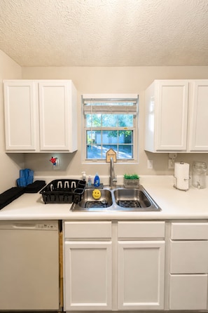 A kitchen with white cabinets, a double sink, a dish rack, and a window with a view of the outside. - 3BR Near Downtown, Zoo Atlanta, & BeltLine (Atlanta)