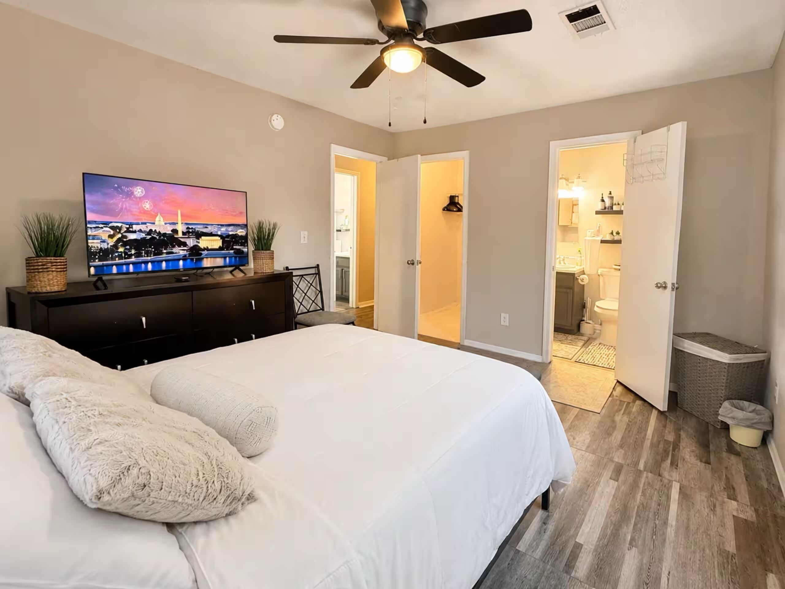 A bedroom with a bed, a TV, a ceiling fan, and a view into the bathroom.