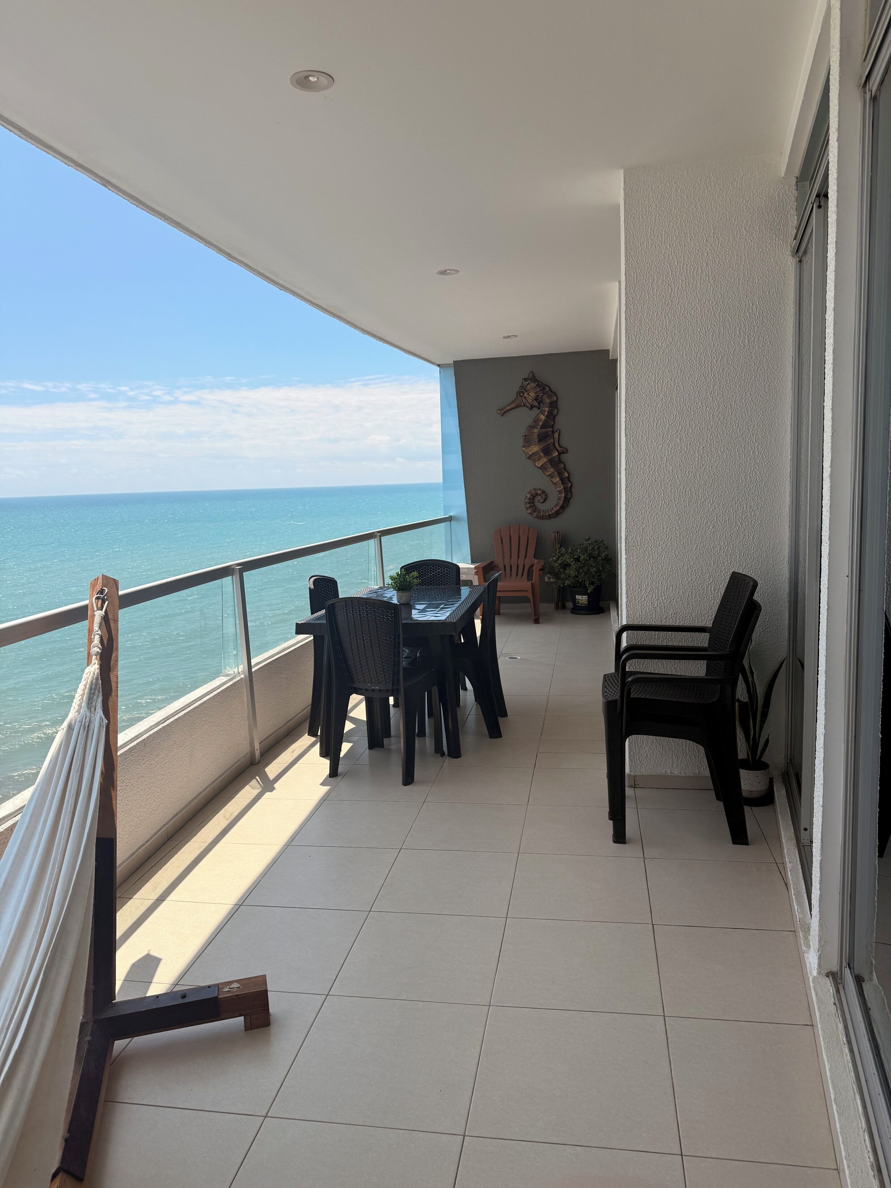 Un balcon avec vue sur l’océan, une table avec des chaises, un hamac et une figurine décorative représentant un hippocampe.