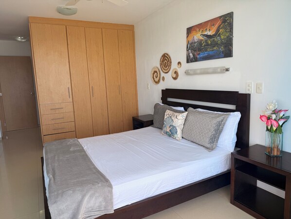 A bedroom with a bed, wooden wardrobe, wall art, and a nightstand with a vase.