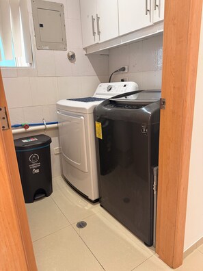 Una cocina compacta con lavadora, refrigerador y contenedor de basura.