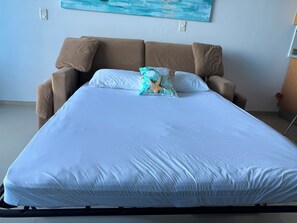 A bed with a white mattress and two pillows, a brown headboard, and a wall-mounted light switch.