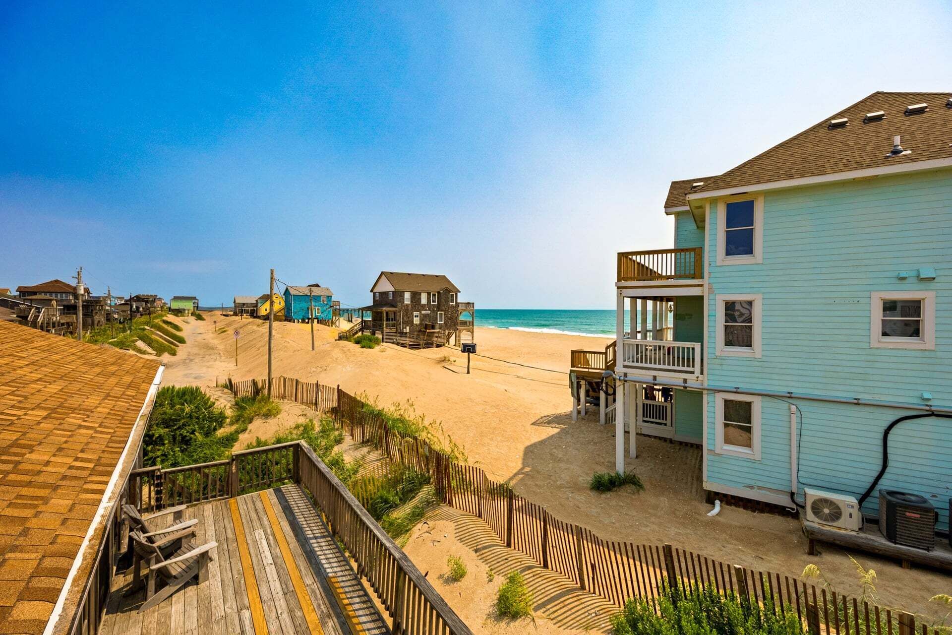 A beachfront property with a wooden deck, a two-story building with a balcony, and a sandy beach in the background.