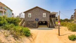 Ein Strandhaus mit Veranda, einer Treppe zum Eingang und einem Schild, das eine Lage am Strand kennzeichnet.