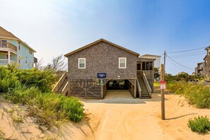 Ein Strandhaus mit Veranda, einer Treppe zum Eingang und einem Schild, das eine Lage am Strand kennzeichnet.