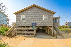 A wooden building with a porch, a staircase, and a sign indicating a beachside vacation rental. - Saltwater Sunrise: Ocean Views & Beach Access (Rodanthe)