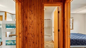 Ein Holzinterieur mit einer sichtbaren Tür zu einem Badezimmer, einem Bett mit gesteppter Bettdecke und einem weißen Regal mit aufgemaltem Dekor.