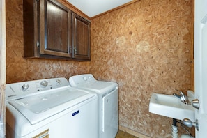 A laundry room with a washing machine, dryer, wooden cabinets, and a sink. - Saltwater Sunrise: Ocean Views & Beach Access (Rodanthe)