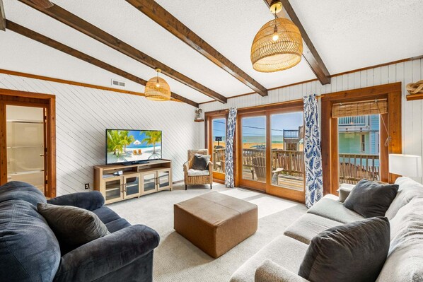 Een woonkamer met een televisie, banken, een salontafel en uitzicht op het strand door grote ramen.