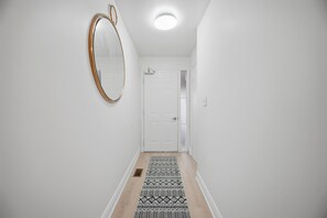 A hallway with a white door, a mirror on the wall, and a patterned rug on the floor.