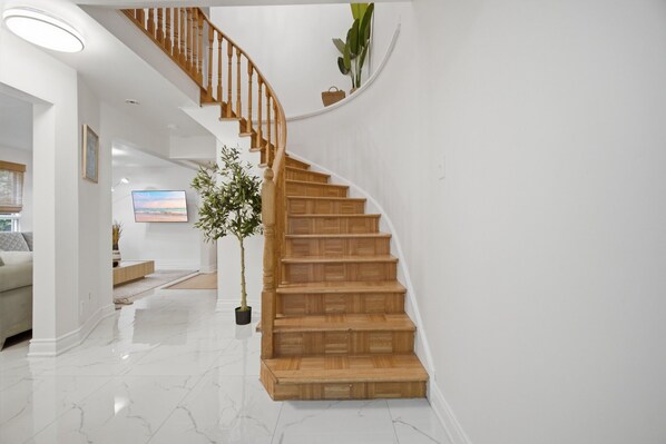 A modern interior with a wooden staircase, a potted plant, and a white wall.