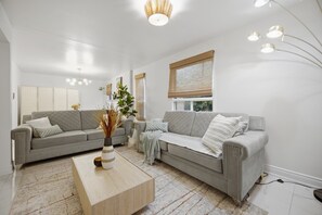 A modern living room with two grey sofas, a wooden coffee table, and a large window with blinds.