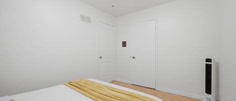 A bedroom with a bed, two doors, a heater, and a white wall.