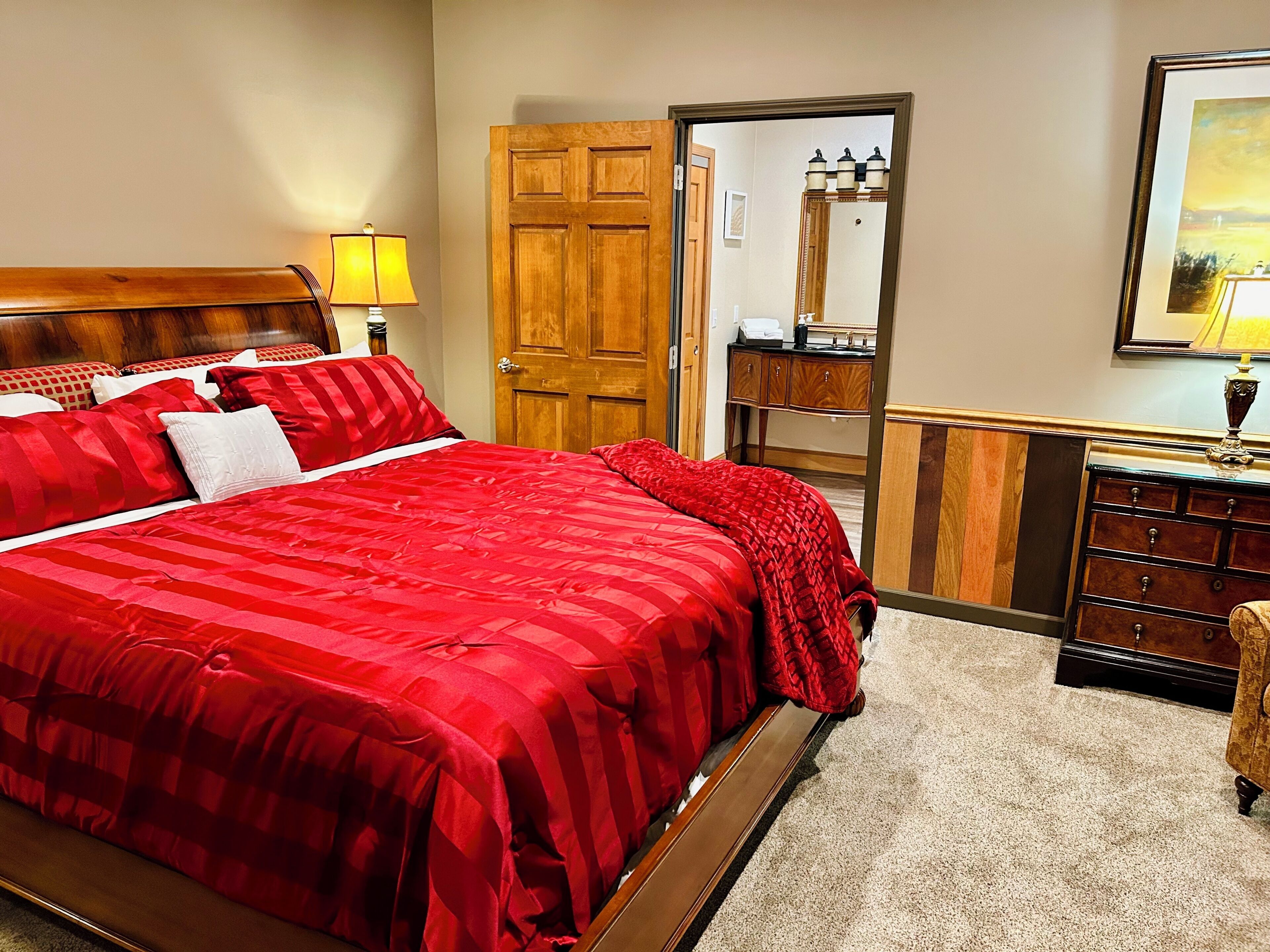 A hotel room with a large bed, wooden headboard, a dresser, a mirror, and a door leading to another room.