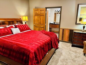 Une chambre d’hôtel avec un grand lit, une tête de lit en bois, une commode, un miroir et une porte donnant sur une autre pièce.