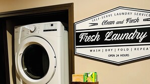 A dual-unit washer and dryer in a laundry room with a sign indicating self-serve laundry services, open 24 hours. - High end 4-bedroom countryside home in Shawano, WI. 2,800 sqft and spacious! (Shawano)