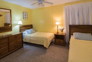 Habitación de hotel con dos camas, ventilador de techo, lámpara de noche, cómoda y espejo.