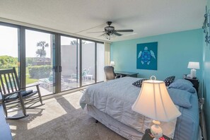 Un dormitorio con cama, escritorio, silla, lámpara y vistas al exterior.