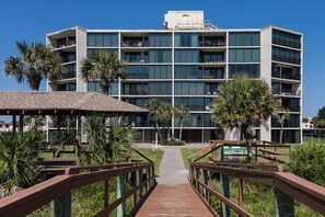 Un hotel de varios pisos con balcones, una galería techada y palmeras.