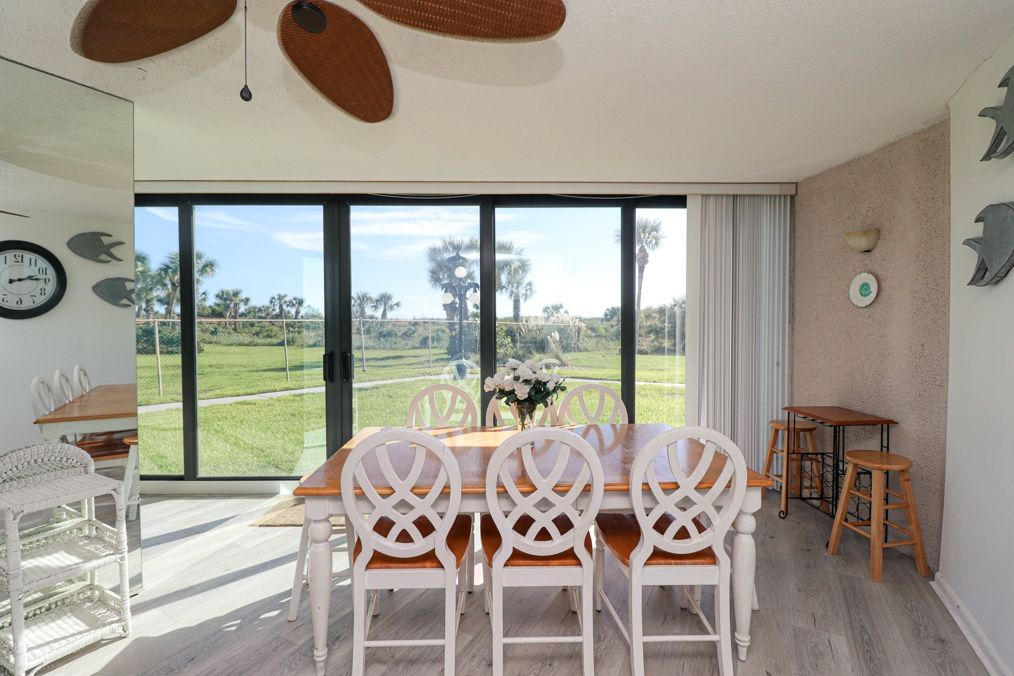 Un coin repas avec une grande fenêtre, des chaises blanches, une table en bois et une vue sur un champ verdoyant.