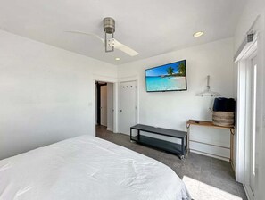A bedroom with a bed, a ceiling fan, a TV on a stand, a door, and a wall-mounted picture. - Beach FRONT | 180 degree VIEWS | REVIEWS!!! (Crystal Beach)