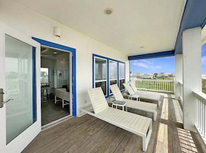 A covered outdoor area with wooden flooring, white lounge chairs, and a view of the landscape. - Beach FRONT | 180 degree VIEWS | REVIEWS!!! (Crystal Beach)