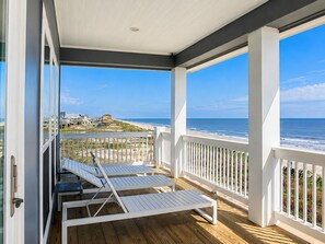 A covered porch with white railings and two white lounge chairs, overlooking a beach with houses in the background. - Beach FRONT | 180 degree VIEWS | REVIEWS!!! (Crystal Beach)