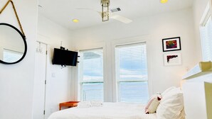 Un dormitorio con una cama, ventilador de techo, televisor y dos ventanas con persianas.