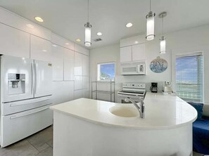 A modern kitchen with white cabinetry, a central island with a sink, and overhead lighting. - Beach FRONT | 180 degree VIEWS | REVIEWS!!! (Crystal Beach)