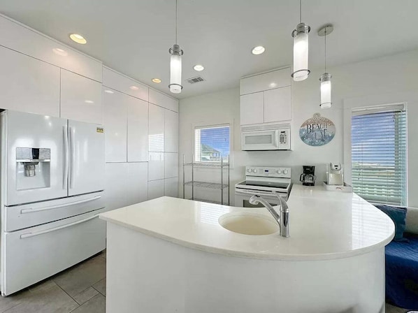 A modern kitchen with white cabinetry, a central island with a sink, and overhead lighting. - Beach FRONT | 180 degree VIEWS | REVIEWS!!! (Crystal Beach)