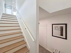 A staircase with wooden steps and white walls, leading to a door. There is a framed picture on the wall. - Beach FRONT | 180 degree VIEWS | REVIEWS!!! (Crystal Beach)