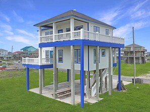 A two-story house with a balcony on the upper floor, elevated on stilts, surrounded by grass. - Beachfront Home w/ 180 Degree Views | Private (Crystal Beach)